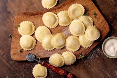 Tahta kesme tahtasının üzerinde un ve mutfak gereçleri ile ev yapımı taze ravioli makarna.