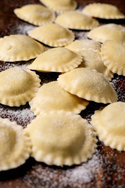 Tahta kesme tahtasına un serpiştirilmiş taze ev yapımı ravioli makarna. Geleneksel İtalyan mutfağı hazırlama süreci.