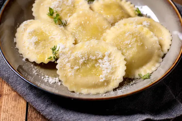 Seramik kasede servis edilen nefis ev yapımı ravioli makarna rendelenmiş parmesan peyniri ve ahşap masada taze kekik otları.
