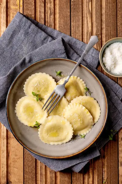 Seramik tabakta servis edilen nefis ev yapımı ravioli makarna ve ahşap masa arkasında çatallı parmesan peyniri otları.