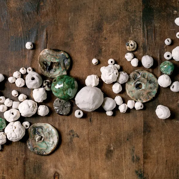 Çeşitli şekiller ve renkler el yapımı seramik boncuklar, jöleli ve parlatılmamış. Hobi, mücevher montajı, mücevher. Atölye fikri. Koyu ahşap arkaplan, üst manzara.