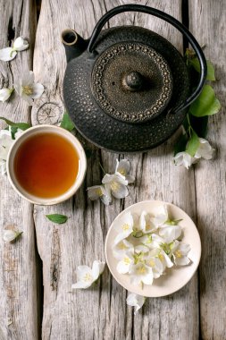 Geleneksel dökme demir çaydanlık sıcak çay fincanı ve kırsal ahşap masada beyaz yasemin çiçekleri dinlenmek için huzurlu zen atmosferi yaratır.