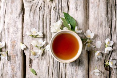 Beyaz yasemin çiçekleriyle çevrili bir fincan çayı. Kırsal ahşap arka plan manzaralı. Bahar çiçekleriyle doğal bitkisel içecekler.