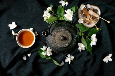 Geleneksel çay seremonisi, dökme demir çaydanlık çayı, yasemin çiçekleri ve koyu kumaş arka planda doğal malzemelerle yapılır.