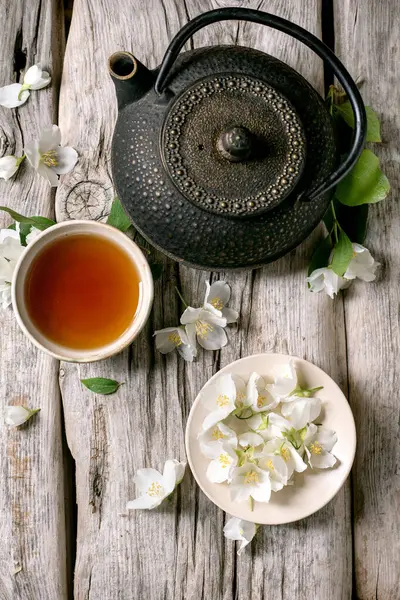 Geleneksel dökme demir çaydanlık sıcak çay fincanı ve kırsal ahşap masada beyaz yasemin çiçekleri dinlenmek için huzurlu zen atmosferi yaratır.