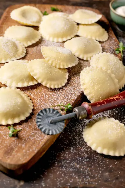 Geleneksel İtalyan pişirme hazırlıkları için un tozlu makarna kesme aleti ile ahşap kesme tahtasına dizilmiş taze ev yapımı ravioli makarna.