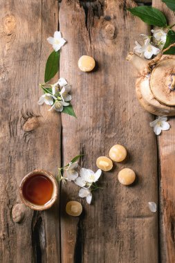 Beyaz yasemin çiçekleri ve mochi toplarıyla süslenmiş kırsal ahşap masa üzerinde cam çaydanlık ve fincanla geleneksel çay seti.