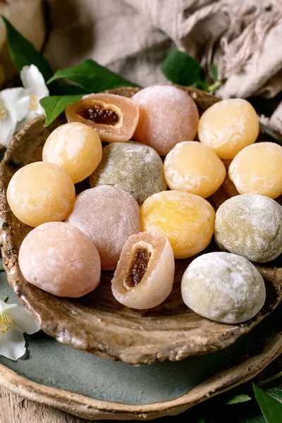 Beyaz çiçekler ve yeşil yapraklarla süslenmiş ahşap tabakta tatlı dolgulu geleneksel Japon mochi pirinç kekleri.