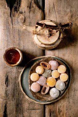 Seramik kasede renkli Japon mochi tatlısı çaydanlık ve kırsal ahşap arka planda çay fincanı. Geleneksel tatlı sunumu.