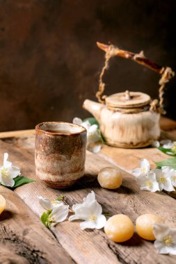 Seramik çaydanlık ve fincan, beyaz yasemin çiçekleri ve geleneksel Japon mochi şekerleriyle süslenmiş ahşap masa üzerinde huzurlu çay seremonisi atmosferi yaratıyor.