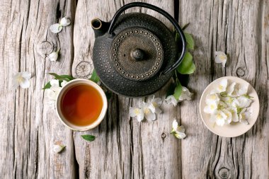 Kırsal ahşap arka planda sıcak çay yasemin çiçekli demir çaydanlık. Doğal çiçeklerle süslenmiş geleneksel Asya çay seremonisi.