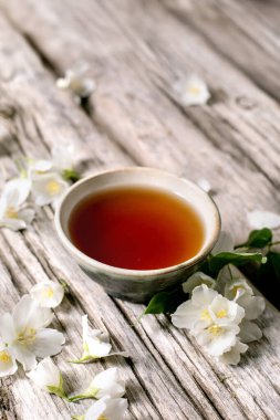 Kırsal ahşap masa üzerinde yasemin çiçekli bir fincan bitki çayı. Çiçek süslemeli doğal içecek sahnesi.