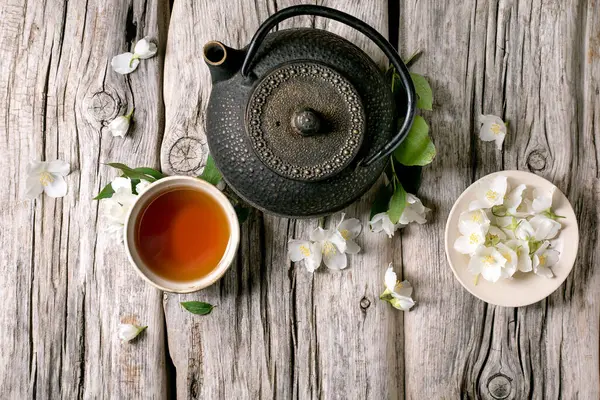 Kırsal ahşap arka planda sıcak çay yasemin çiçekli demir çaydanlık. Doğal çiçeklerle süslenmiş geleneksel Asya çay seremonisi.