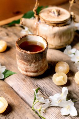 Seramik çaydanlık ve fincan, beyaz yasemin çiçekleri ve geleneksel Japon mochi şekerleriyle süslenmiş ahşap masa üzerinde huzurlu çay seremonisi atmosferi yaratıyor.