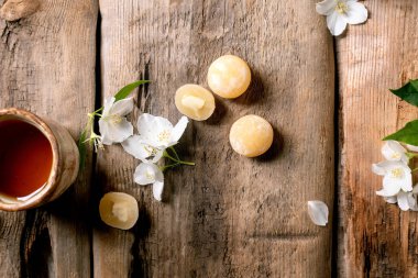 Beyaz yasemin çiçekleri ve geleneksel Asya tatlısı mochi toplarıyla süslenmiş kırsal ahşap masa üzerindeki seramik çay fincanı.