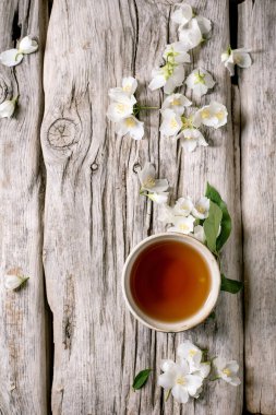 Kırsal ahşap arka planda beyaz çiçekli yasemin çayı. Doğal bitkisel içecek. Taze çiçeklerle yıpranmış ahşap yüzeye serpilmiş çay fincanı..