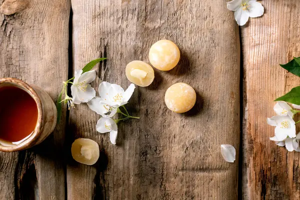 Beyaz yasemin çiçekleri ve geleneksel Asya tatlısı mochi toplarıyla süslenmiş kırsal ahşap masa üzerindeki seramik çay fincanı.