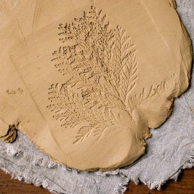 Seramik dekorasyonu. Yuvarlak yuvarlanmış sarı kil levhanın üzerinde eşkıya dalı izi olan tahta masa üzerindeki kaba kumaş uzanıyor. Eko dekor. Seramik atölyeler, el heykelleri. Üst görünüm