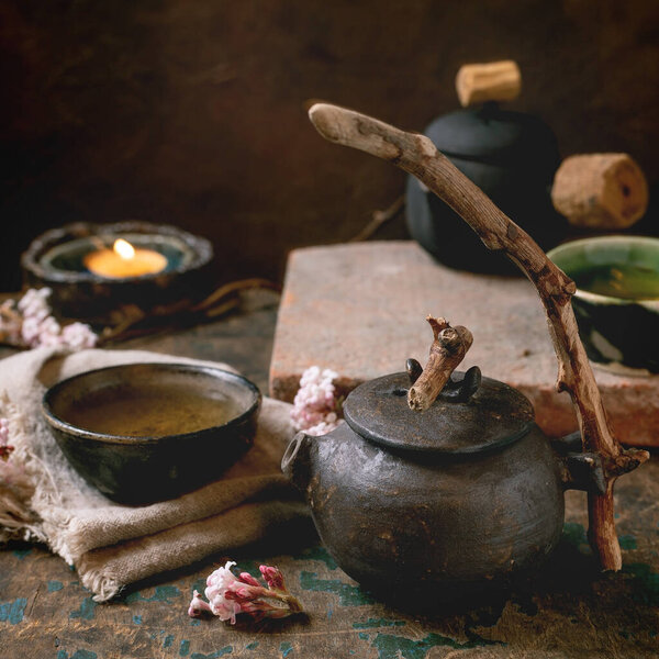 Chinese Tea Ceremony. Two traditional handmade ceramic black teapot with wooden handle on dark wooden table. Ceramic teacups and pink spring flowers, burning tea candle. Tea ceramics