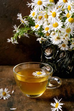 Cam bardak bitkisel papatya çayı ve beyaz papatya çiçekleri ahşap masadaki vazoda. Taze çiçek desenli doğal sağlık içeceği konsepti.