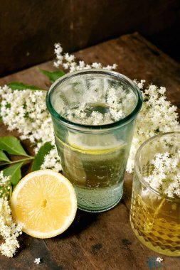 Taze limon dilimi ve ahşap arka planda beyaz elder çiçeği çiçekleri ile birlikte cam içinde elderflower içeceği tazeleniyor. Doğal bitkisel içecek konsepti.