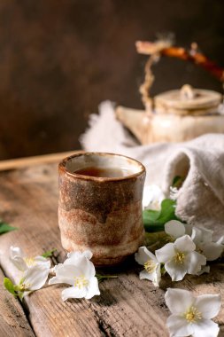 Seramik çay fincanı ve ahşap masada sıcak çay beyaz bahar çiçeği çaydanlığı. Doğal dekorasyonlu geleneksel oryantal çay seremonisi.