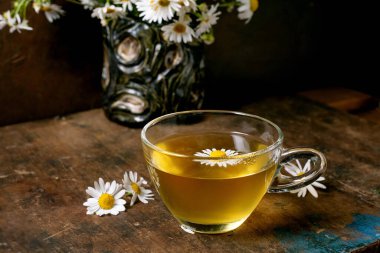 Kırsal ahşap masada papatya çiçekleriyle süslenmiş cam bardak bitkisel papatya çayı. Çiçek düzenleme geçmişi olan doğal sağlık içeceği konsepti.