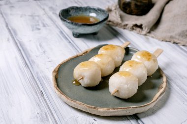 Tahta şiş üzerinde Japon dango pirinç köftesi seramik tabakta servis edilir bal soslu geleneksel Asya tatlısı beyaz ahşap masada.