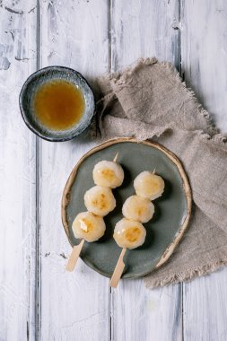 Japon dango köfteleri seramik tabakta çay kâsesi ahşap çubuklarla beyaz ahşap arka planda keten peçete. Geleneksel Asya tatlısı
