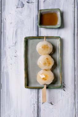Japon dango pirinç köfteleri ahşap şiş üzerinde servis edilir seramik tabakta geleneksel Asya tatlısıyla birlikte beyaz ahşap arka planda