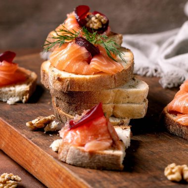 İnce dilimlenmiş somon filetosu, pancar dilimleri, ceviz, balzamik sirke ve tahtadan yapılmış taze buğday ekmeği ile sandviç. Kahverengi arka plan. Yılın Renkleri 2025.