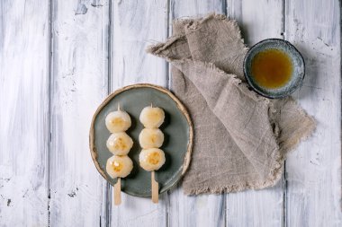 Geleneksel Japon dango köfteleri seramik tabakta kırsal beyaz ahşap masa üzerinde keten peçeteli yeşil çayla servis edilir.