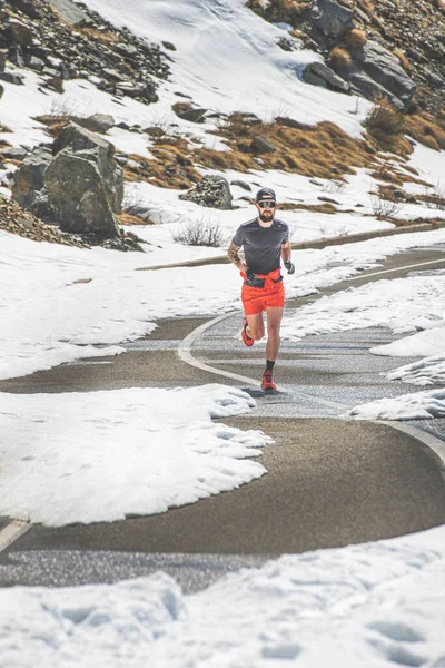 男のアスリートは高山の峠を越えて雪と春に道路で訓練を実行します — ストック写真