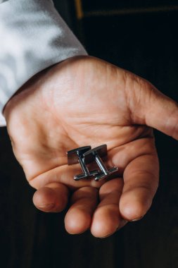 Gömlekli bir adam elinde şık kol düğmeleri tutar, yakın plan. Damadın tören için sabah hazırlığı. Yüksek kalite fotoğraf. Yüksek kalite fotoğraf