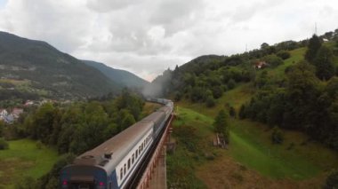 Dizel tren nehir yamacı boyunca uzanan manzaralı araziden demiryolunun her iki tarafındaki yeşil çimlerin arasından geçer. Havadan görüş ve trenin izini sürme. Yüksek kalite 4k görüntü