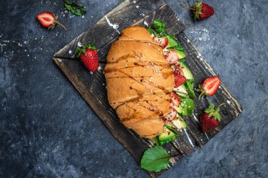 Avokado, çilekli, peynirli, peynirli kruvasan sandviçi susam ve kimyon serpiştirilmiş taze salata lezzetli kahvaltı veya atıştırmalık Keto diyet vejetaryen yemeği..