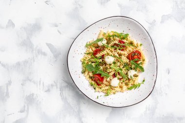 İtalyan soğuk makarna salatası. Fusilli, domates, mozzarella, zeytin, roka. Koyu arkaplanda makarna alla caprese, Restoran menüsü, diyet, yemek kitabı tarifi üst görünümü,