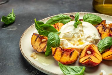 Burrata soft cheese and grilled peaches with basil and pine nuts, drizzled honey, Food recipe background. Close up,