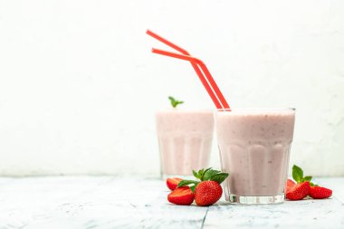 Çilekli smoothie ya da meyveli milkshake ve beyaz beton arka planda cam kavanozda yoğurt. Sağlıklı vejetaryen içeceği. metin için yer, üst görünüm,