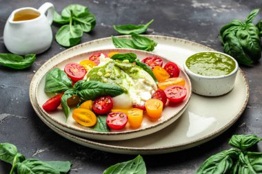 Salad burrata cheese tomatoes and green pesto. Delicious balanced food concept. superfood concept. Healthy, clean eating. Vegan or gluten free diet. top view.