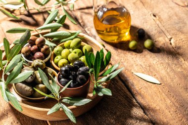 Ahşap kaselerde zeytin, ahşap arka planda cam şişelerde yağ. Sağlıklı ve detoks gıda konsepti.