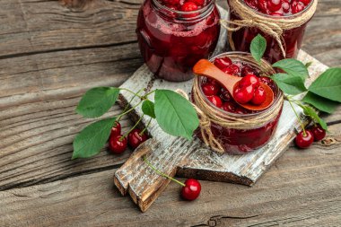 Bir kavanoz kiraz reçeli ve ekşi kiraz. Şerbetli kiraz. Olgun kirazlar. Tatlı kırmızı kirazlar. Ahşap bir arka planda konserve meyve.