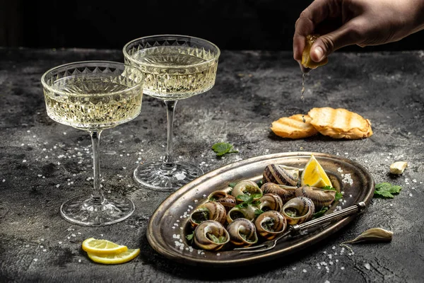 stock image Delicious cooked sea escargo snails with herbs, butter, garlic on metal plate with forks. wine glass. gourmet food. Restaurant menu, Traditional French cuisine,