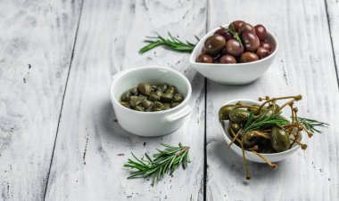 Gri arka planda taze fesleğen yapraklarıyla beyaz tabakta kapari üzümü ve zeytin. Akdeniz atıştırmalıkları. afiş, menü, metin için tarif yeri, üst görünüm.