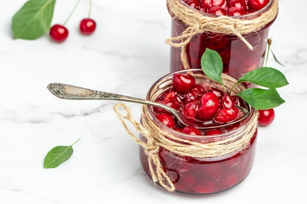 Jar of cherry jam and sour cherries. Berries cherry with syrup. Ripe ripe cherries. Sweet red cherries. Canned fruit on a wooden background.