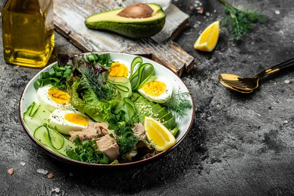 Ketogenic low carbs diet, Plate with keto foods: two eggs, avocado, tuna, cucumber and fresh salad. Healthy fats, clean eating for weight loss. top view.
