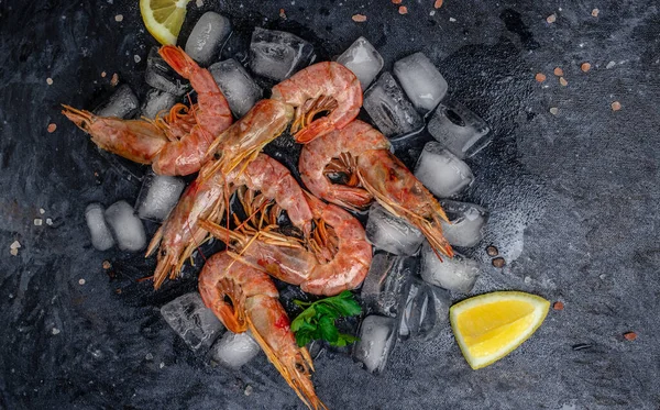 shrimps. wild ocean jumbo shrimps with ice and lemon, seafood shrimps prawns on ice frozen. Long banner format. top view.