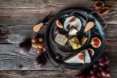 Çeşitli peynir çeşitleri, geleneksel Fransız parçaları, İtalyan ve İspanyol manchego peyniri üzümlü ve incirli ahşap masada servis edilmiş..