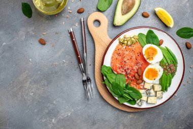 Gri arka planda diyet yemeği, somon, avokado, peynir, yumurta, ıspanak ve fındık. afiş, menü, metin için tarif yeri, üst görünüm.