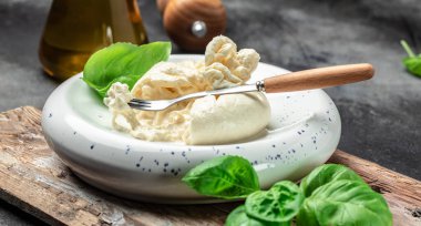 Basil yapraklı burrata peyniri beyaz tabakta koyu arkaplanda. afiş, menü, metin için tarif yeri, üst görünüm.